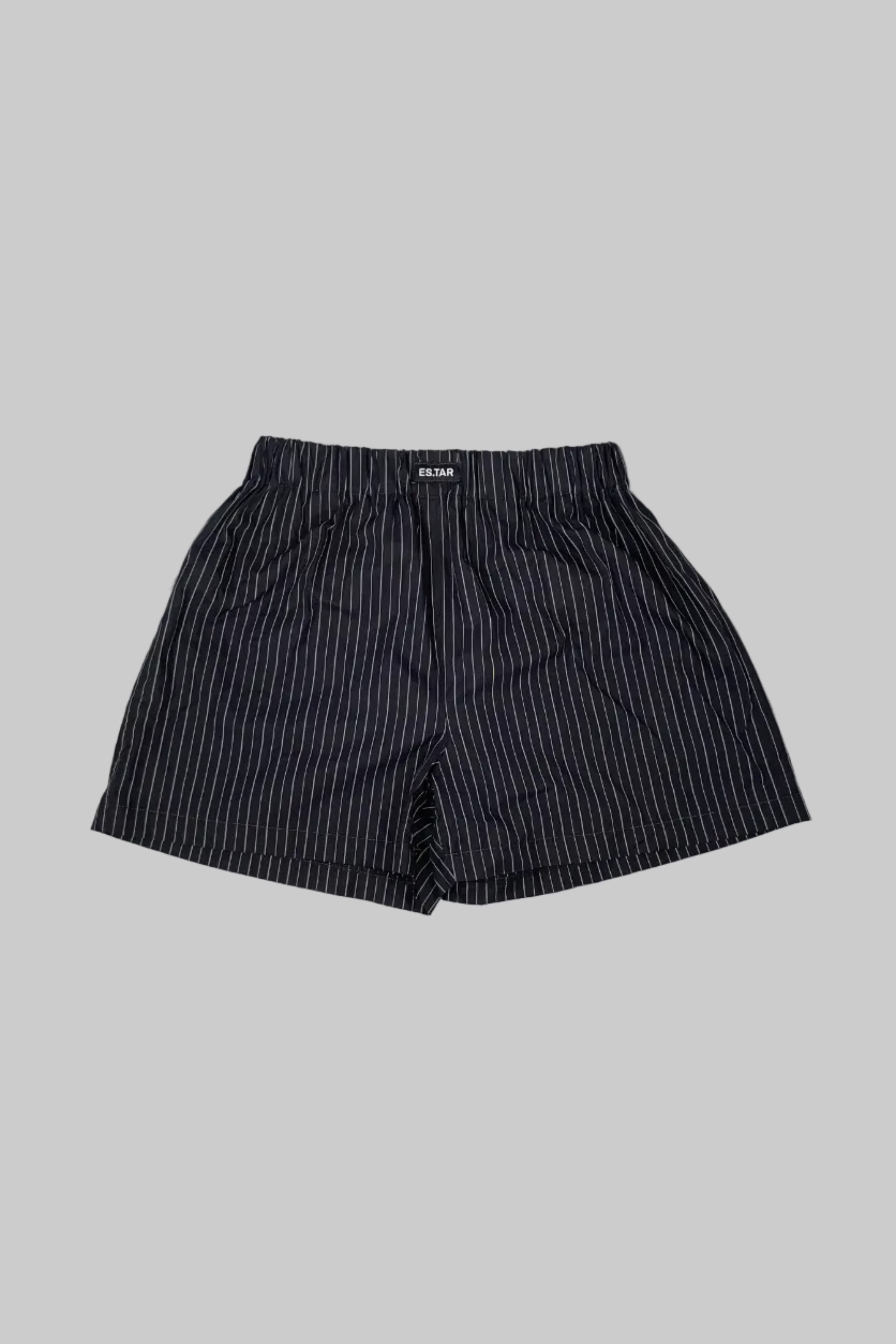 A pair of men's shorts with thin vertical black and white pinstripes, laid flat on a distressed white wooden plank surface.
