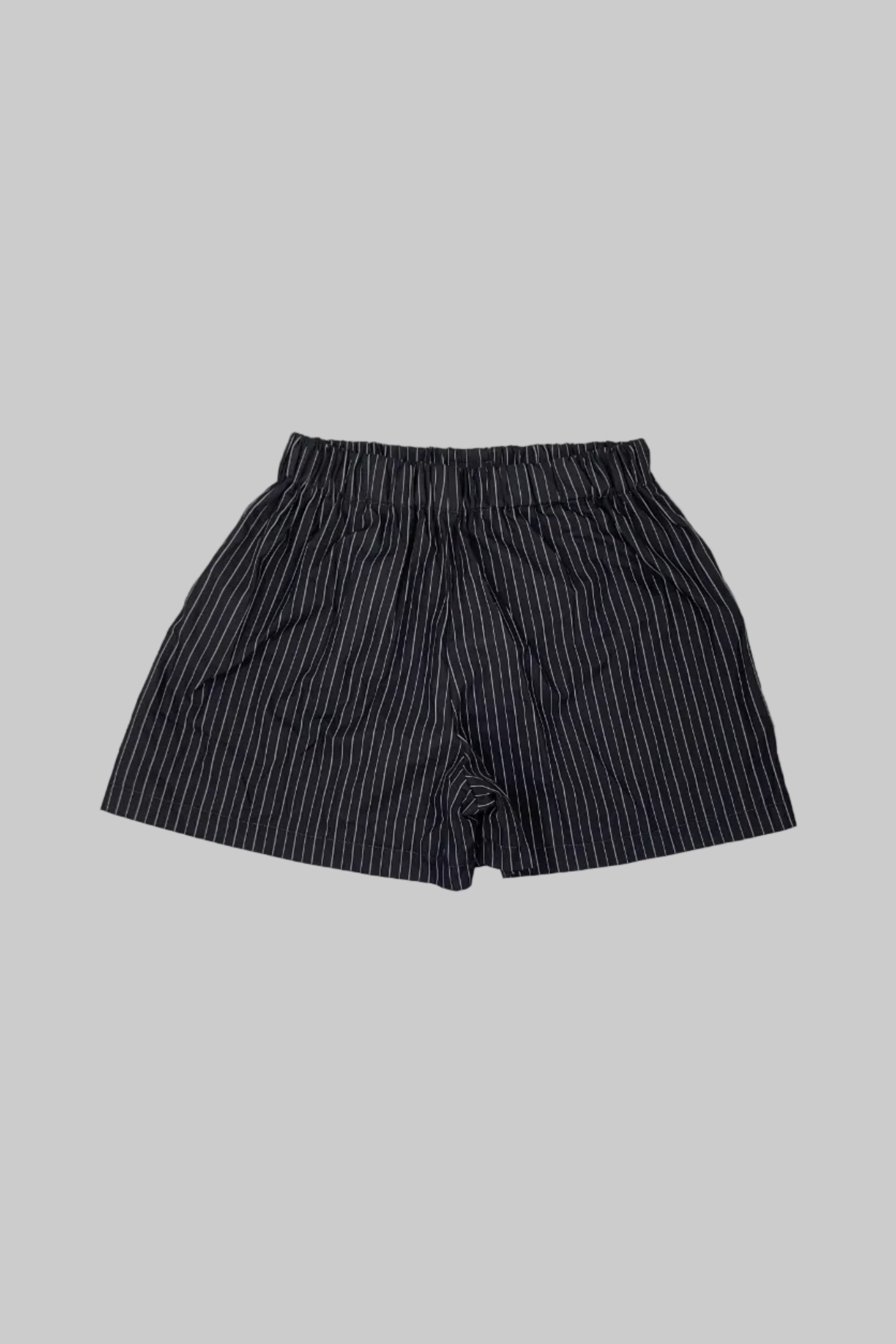 A pair of dark gray and black vertically striped shorts with an elastic waistband, laid flat on a white wooden plank floor.