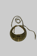 A vintage brass crescent-shaped collar or bib with a matching strap, displayed on a weathered white wooden surface.
