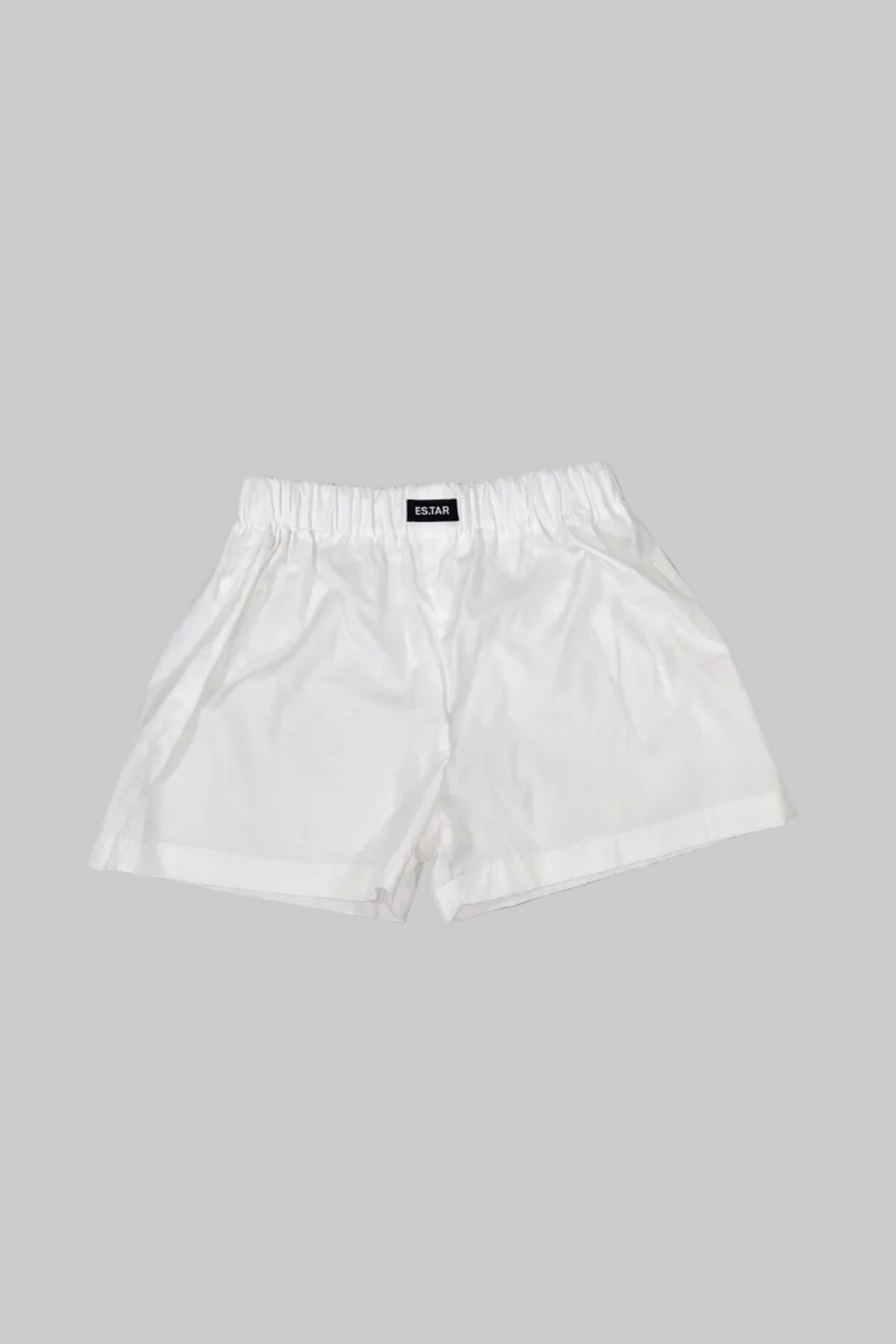 White shorts with an elastic waistband and a small black brand label reading 'TERRA' at the center back waist, laid flat on a gray wooden plank surface.