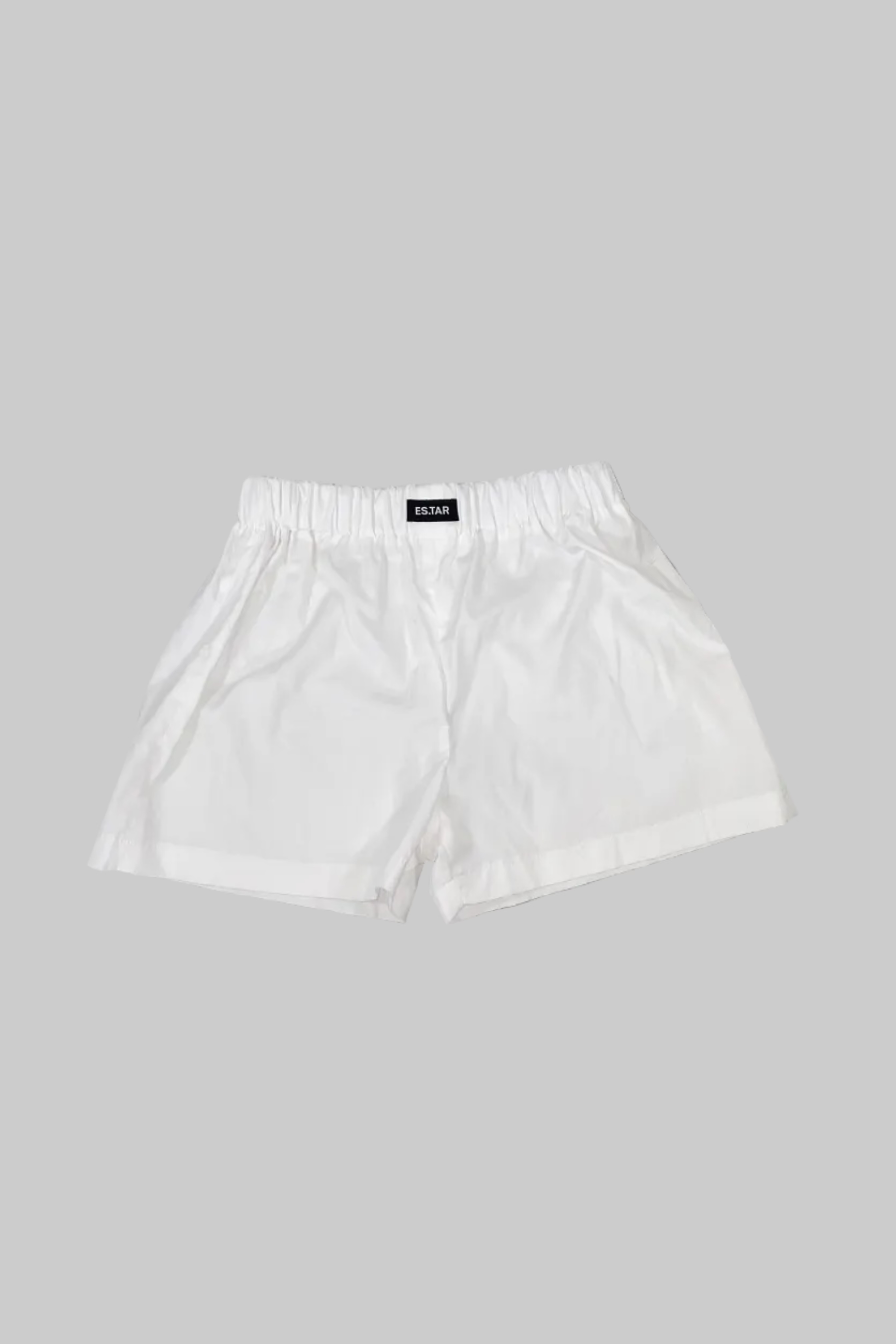 White shorts with an elastic waistband and a small black brand label reading 'TERRA' at the center back waist, laid flat on a gray wooden plank surface.