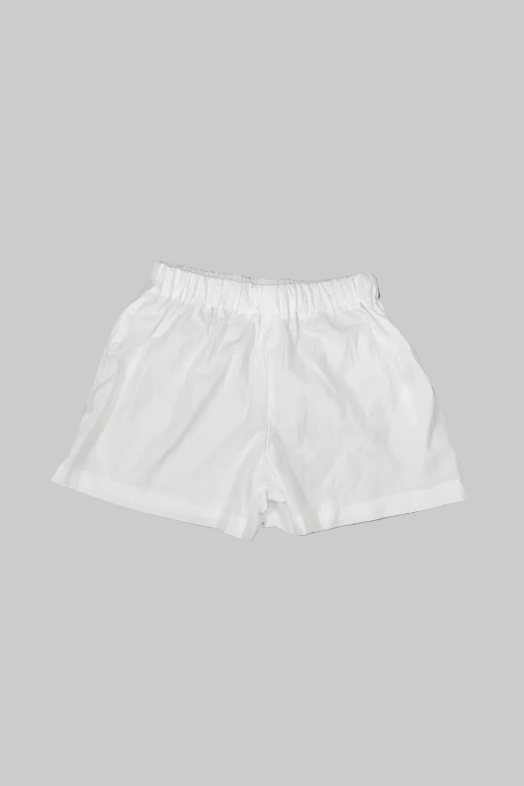 White elastic-waist shorts laid flat on a gray wooden floor.