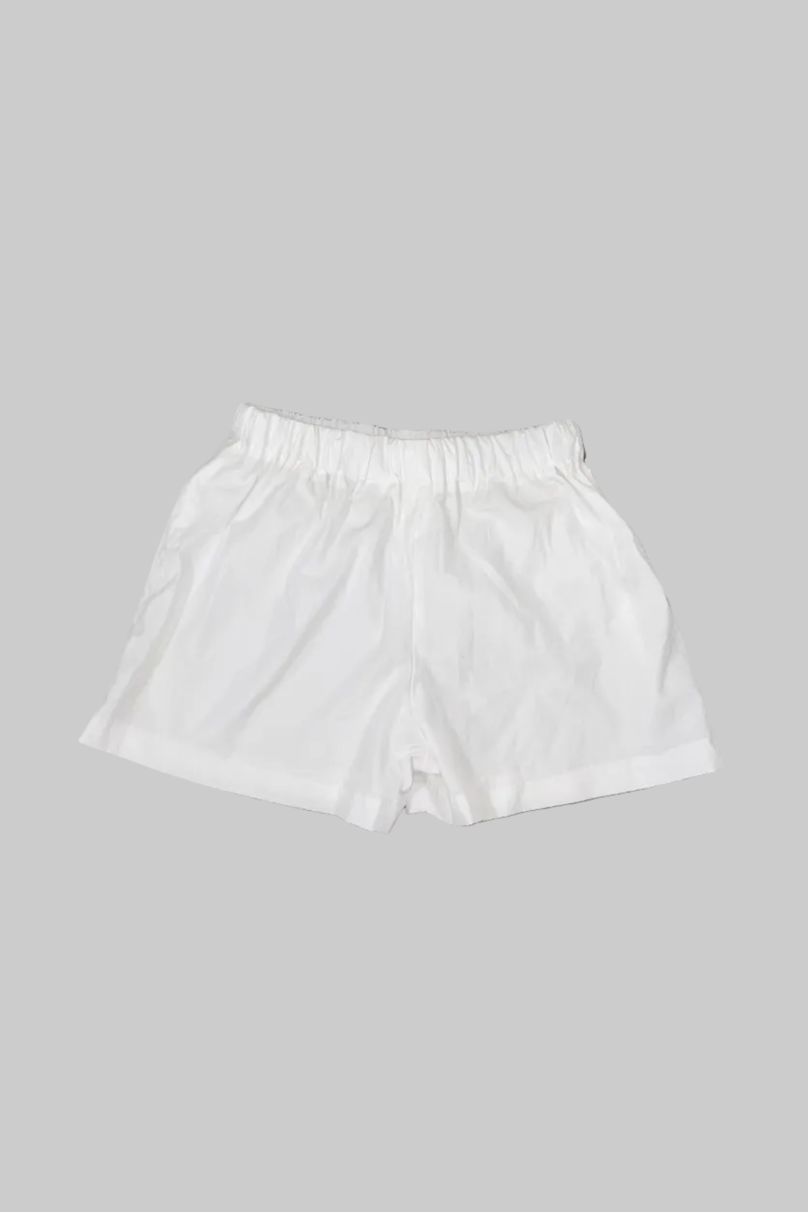 White elastic-waist shorts laid flat on a gray wooden floor.