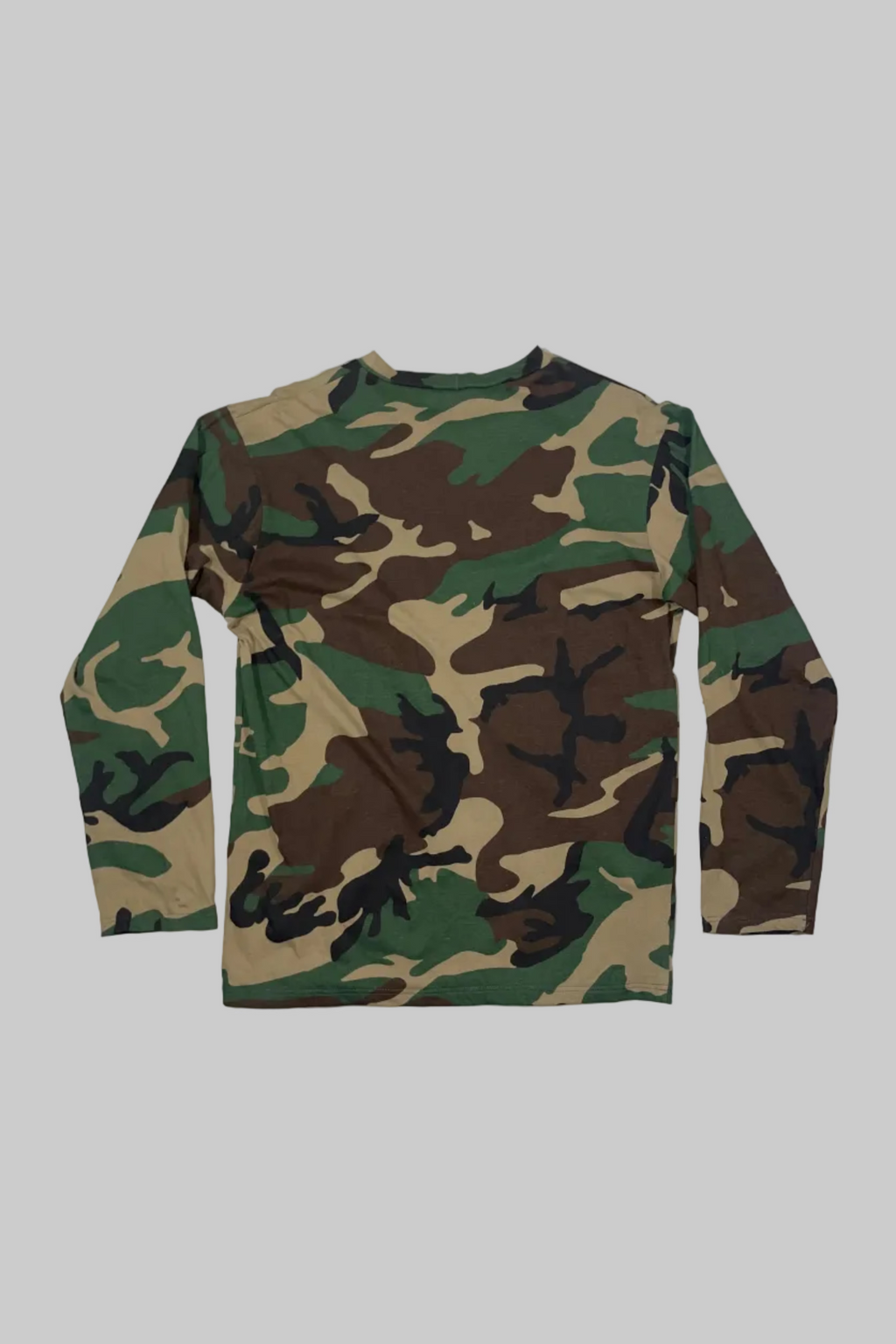 A long-sleeve camouflage shirt in green, brown, black, and tan, laid flat against a white painted wood plank background.
