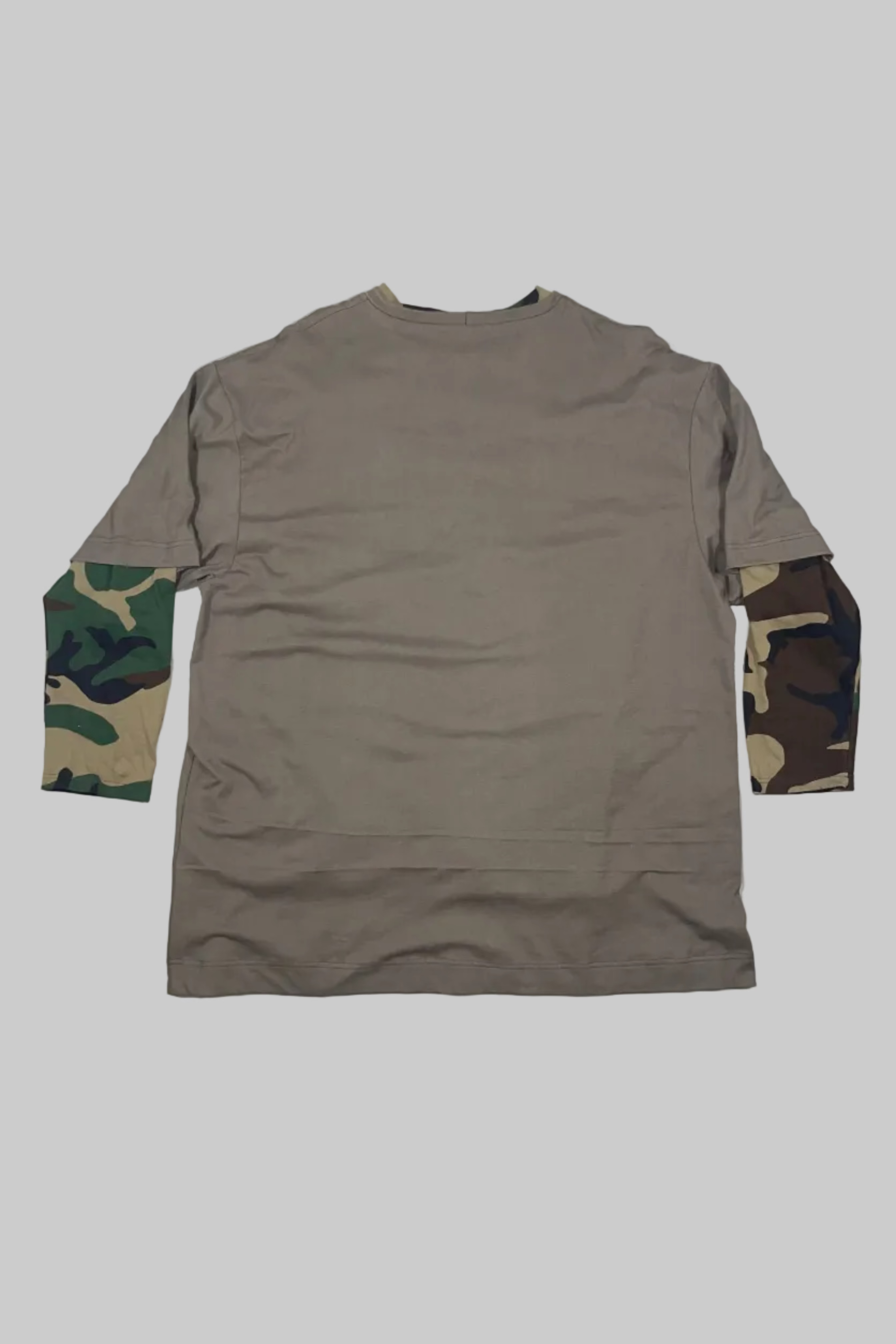 A long-sleeve crewneck shirt laid flat on a white wooden surface, featuring a solid tan body with camouflage-patterned sleeves.