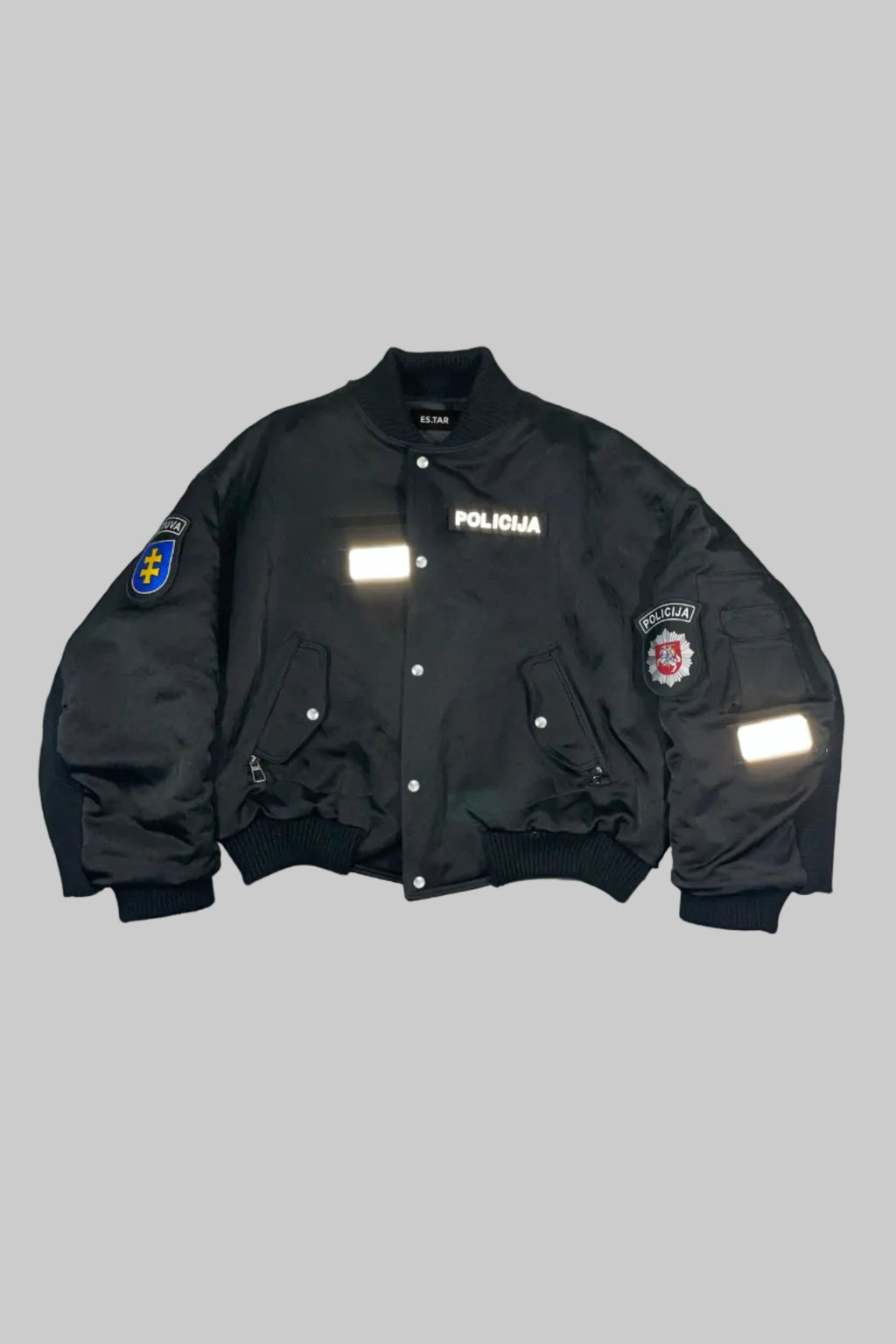 A black bomber jacket with 'POLICIJA' text on the chest and reflective patches on the sleeves, laid flat against a white wooden background.