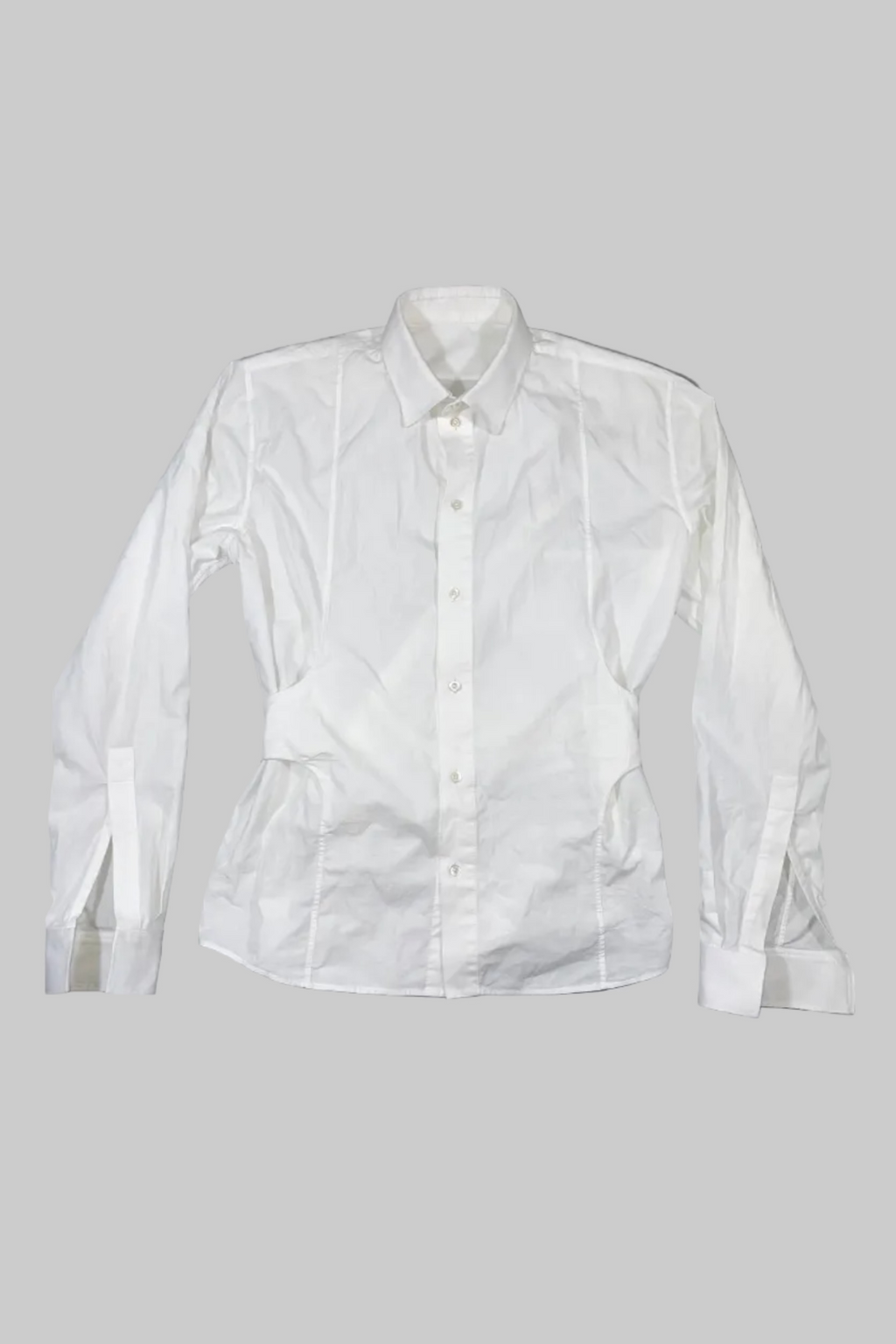 A white long-sleeve button-up shirt with vertical pleat detailing on the front, laid flat against a gray painted wooden plank background.