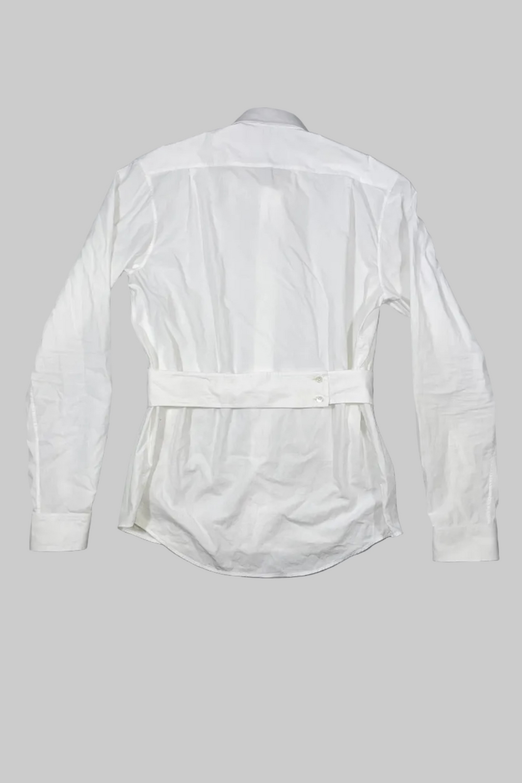 A white long-sleeve button-up shirt with a matching self-tie belt, shown from the back against a gray painted wooden plank background.