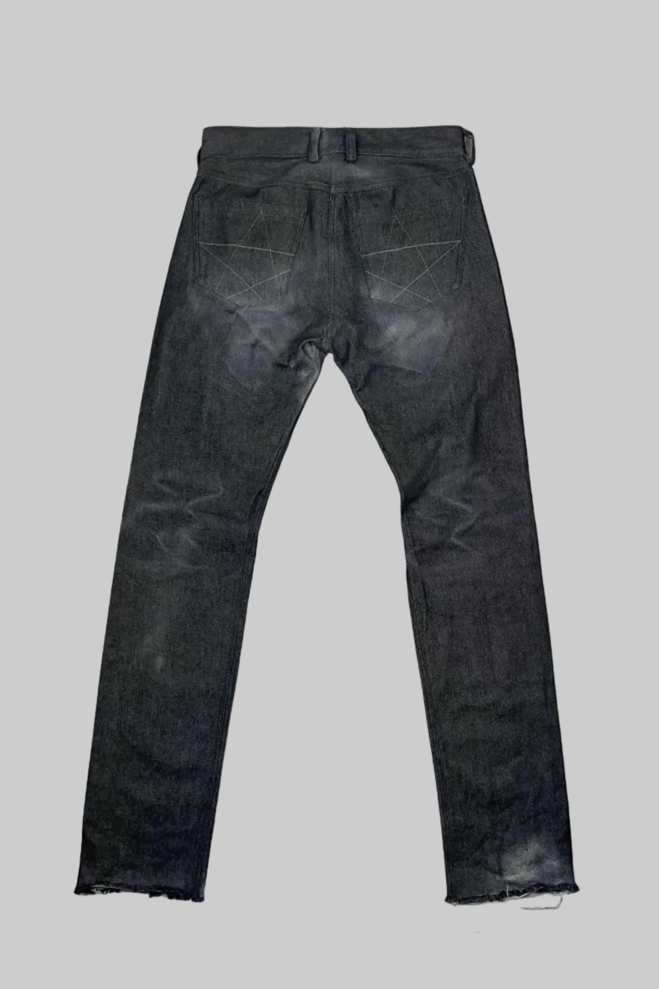 A pair of faded black slim-fit jeans shown from the back, laid flat on a white wooden plank floor.