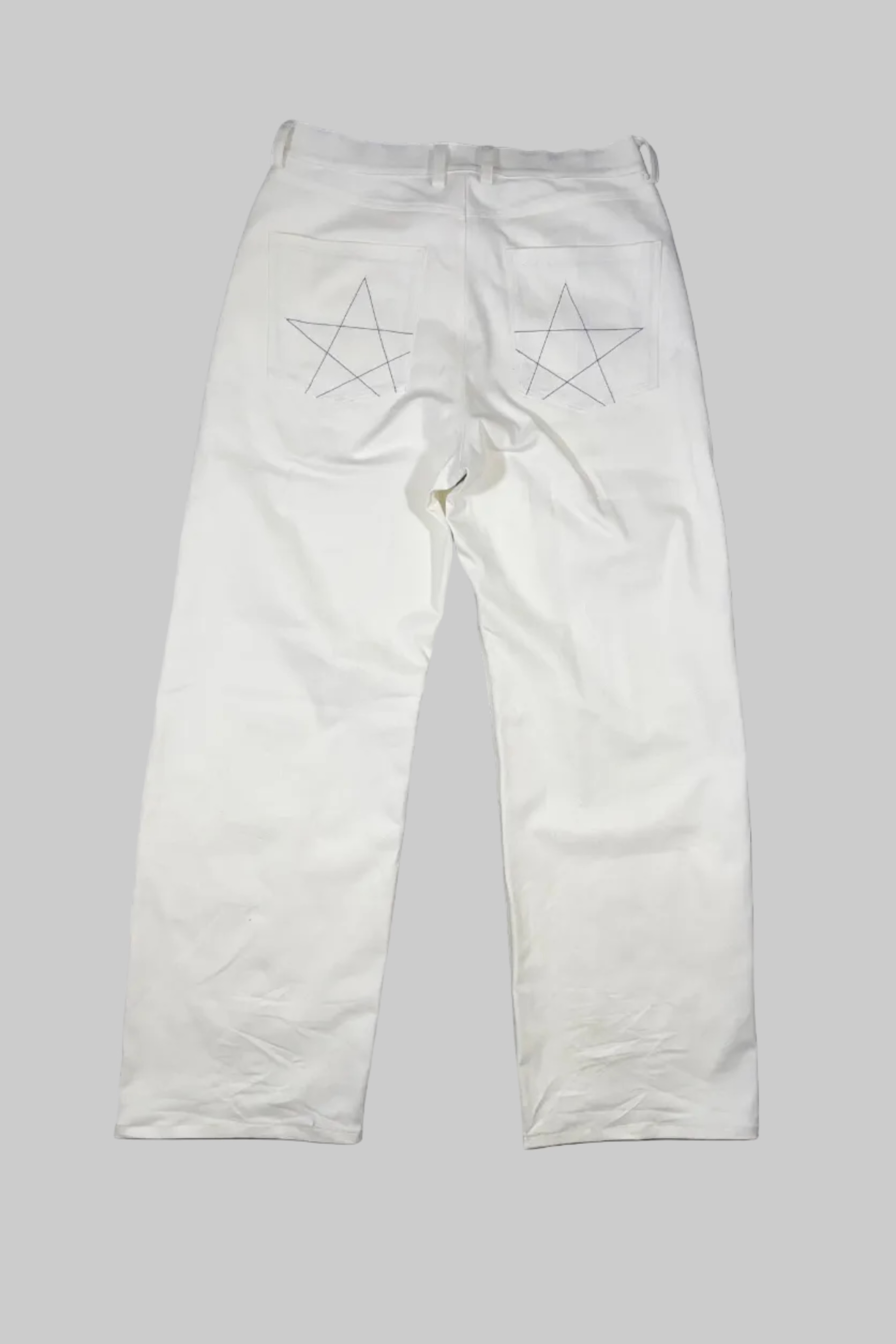 White denim pants laid flat on a gray wooden floor, featuring embroidered star designs on the back pockets.