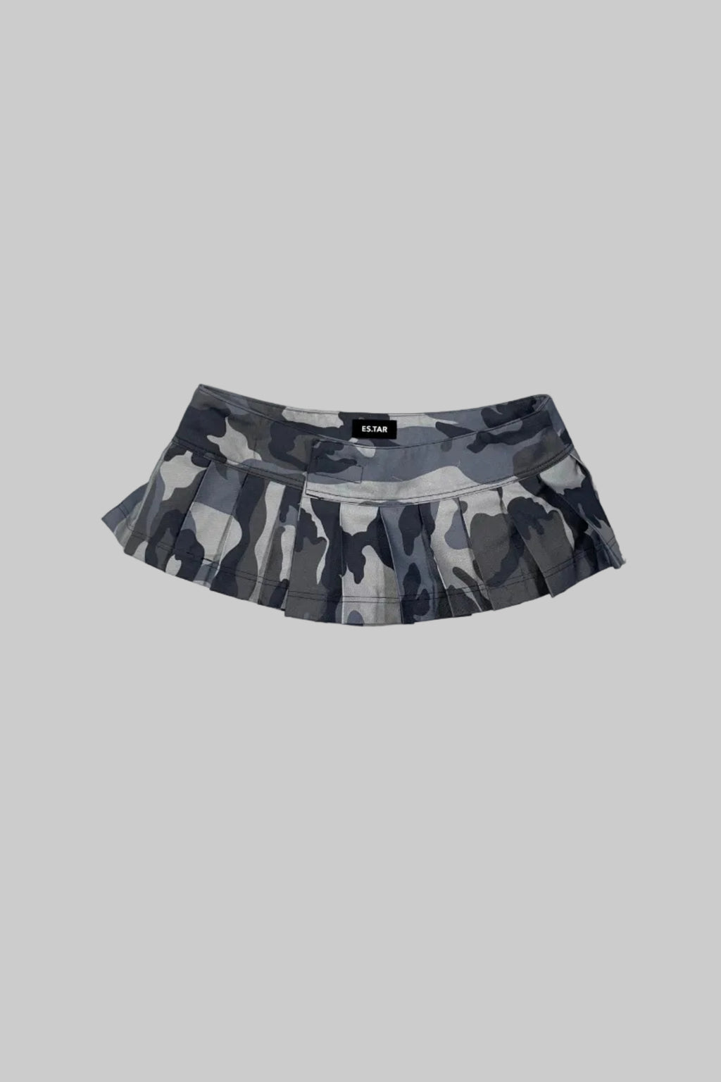 A gray and black camouflage pleated tennis skirt with a black waistband label reading 'ES.TAR', laid flat on a distressed white wooden surface.
