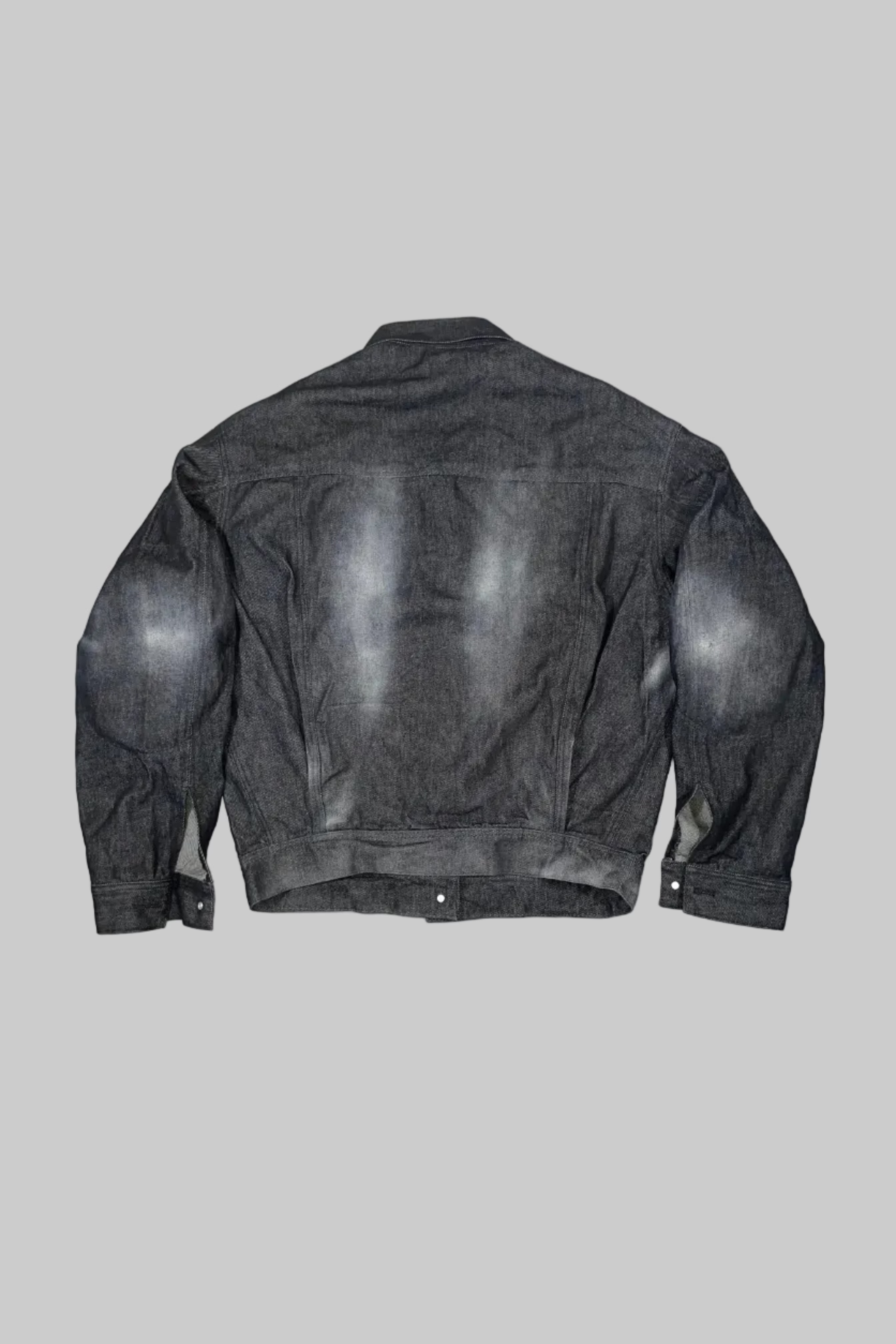 A dark gray washed denim jacket shown from the back, laid flat against a white painted wooden plank background.