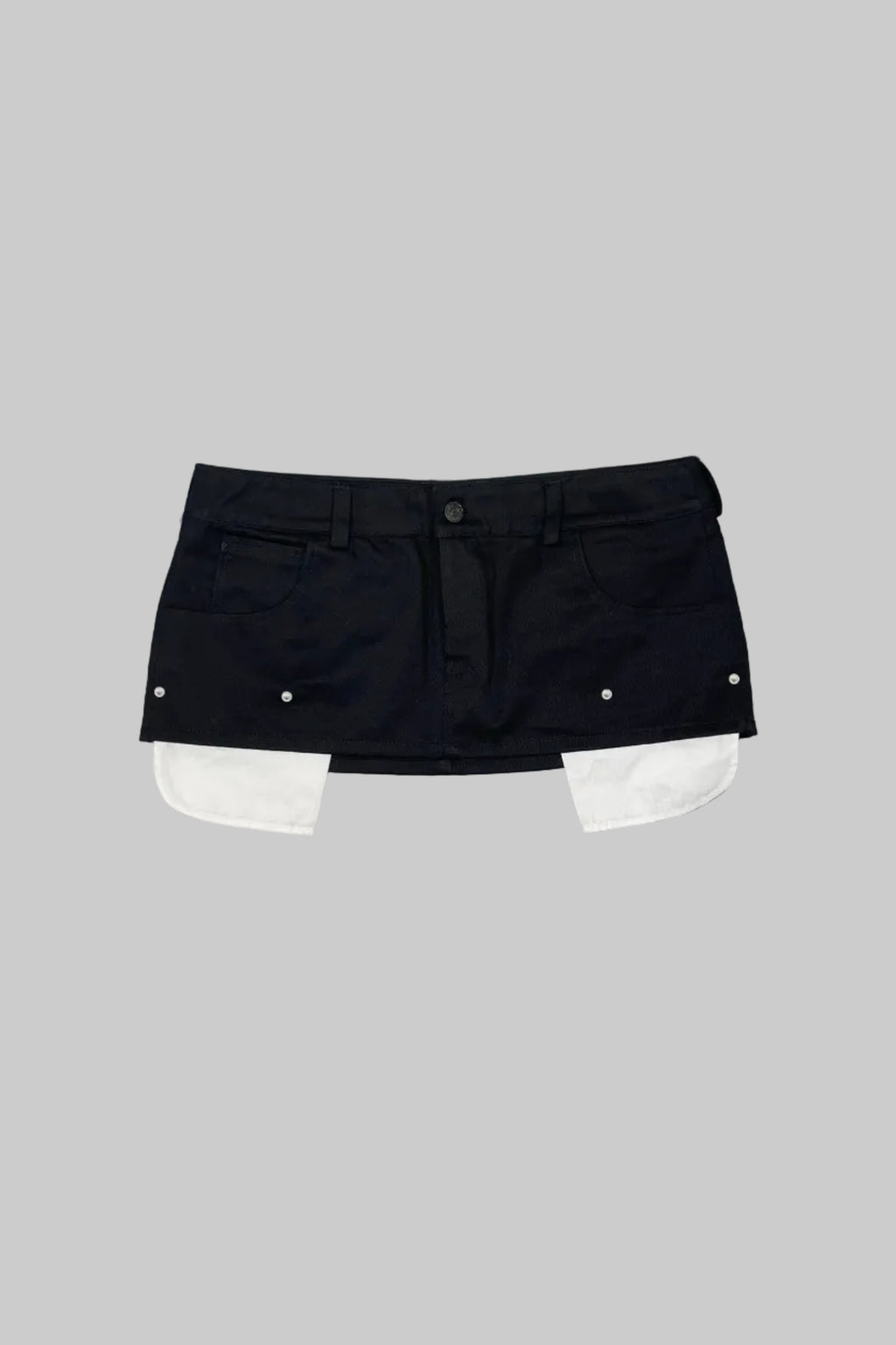 A black denim mini skirt with white contrast panels folded out from the hem, laid flat on a gray wooden plank background.