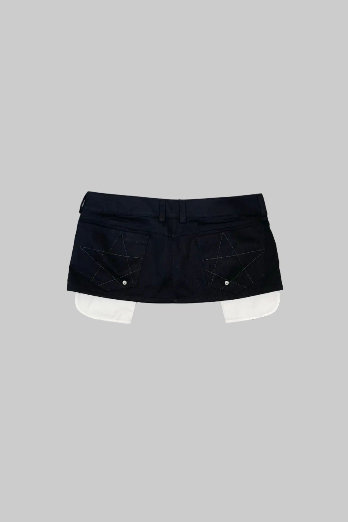 A black denim mini skirt with geometric star embroidery and white contrast stitching, laid flat on a distressed gray wooden floor.