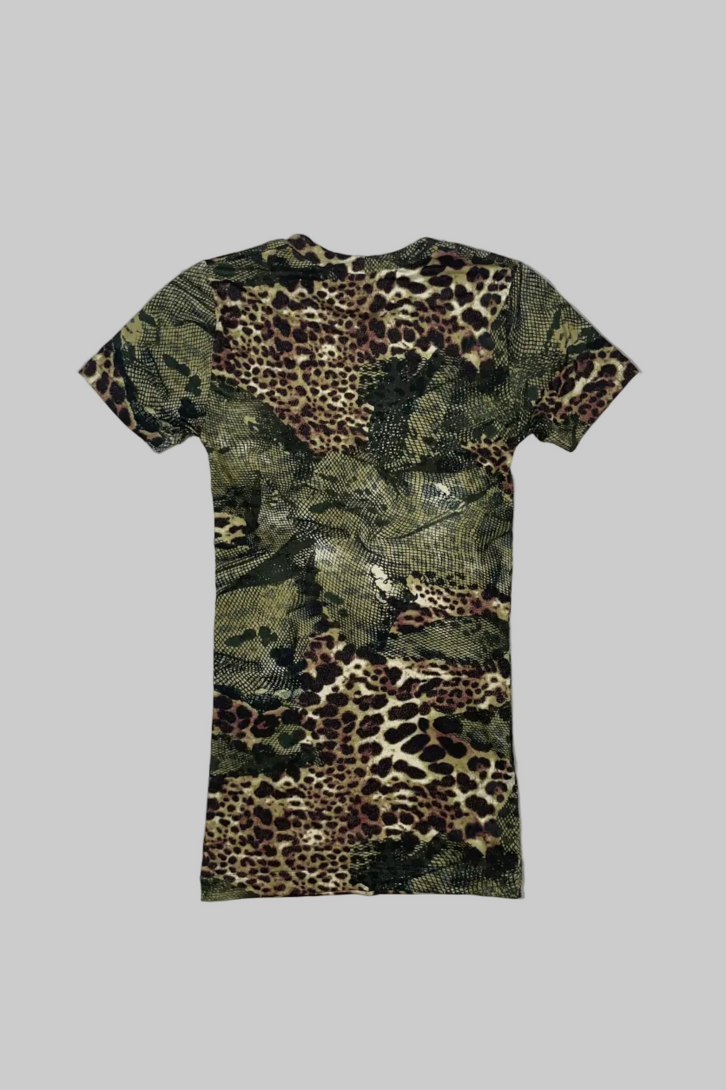 A short-sleeve crewneck t-shirt featuring an all-over leopard print and camouflage pattern in shades of green, brown, black, and beige, laid flat on a white painted wooden plank background.