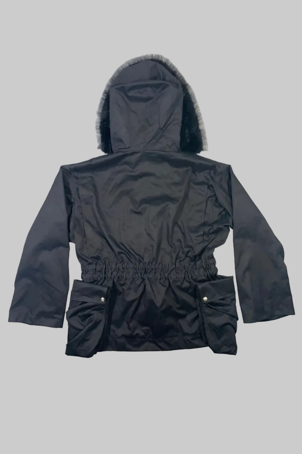A black hooded winter jacket with a faux-fur trimmed hood and an elasticated waist, laid flat on a white wooden plank surface.