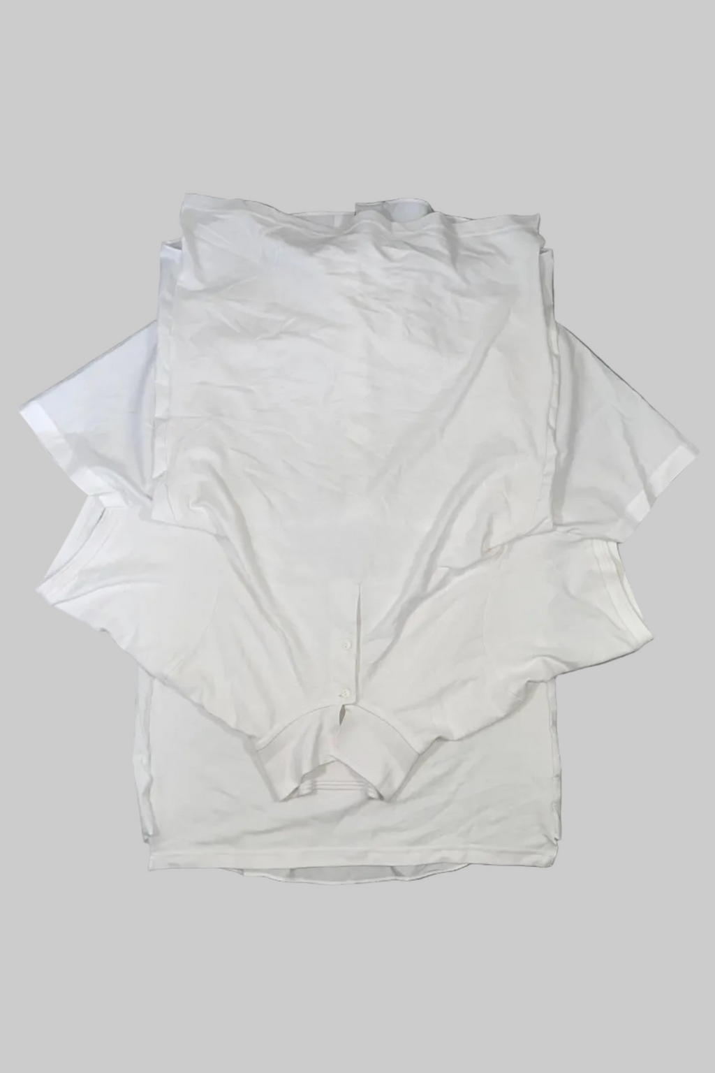 A stack of plain white long-sleeve t-shirts laid flat on a gray wooden floor.