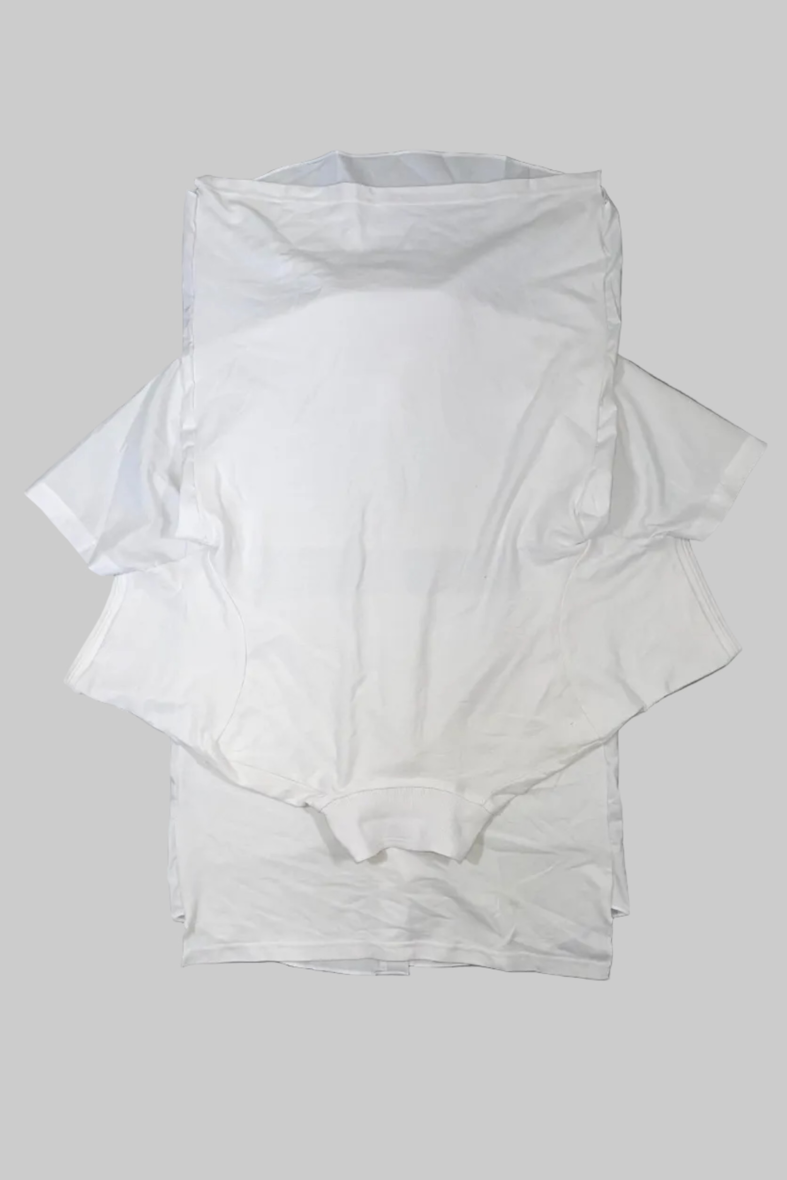 A stack of plain white short-sleeve t-shirts laid flat on a gray wooden plank surface.