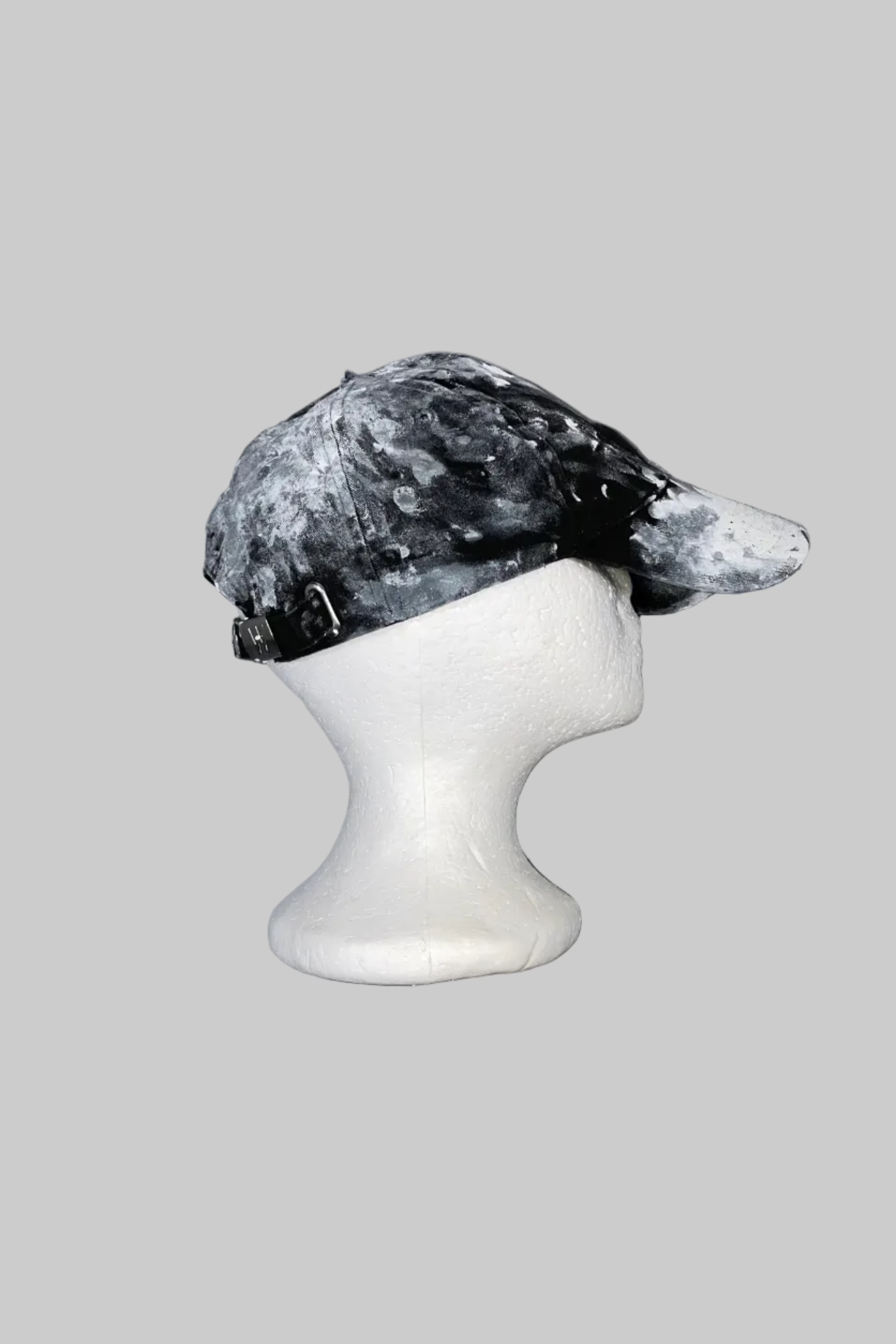 A black and white marbled or mottled cap displayed on a white styrofoam mannequin head, set against a weathered gray wooden background.