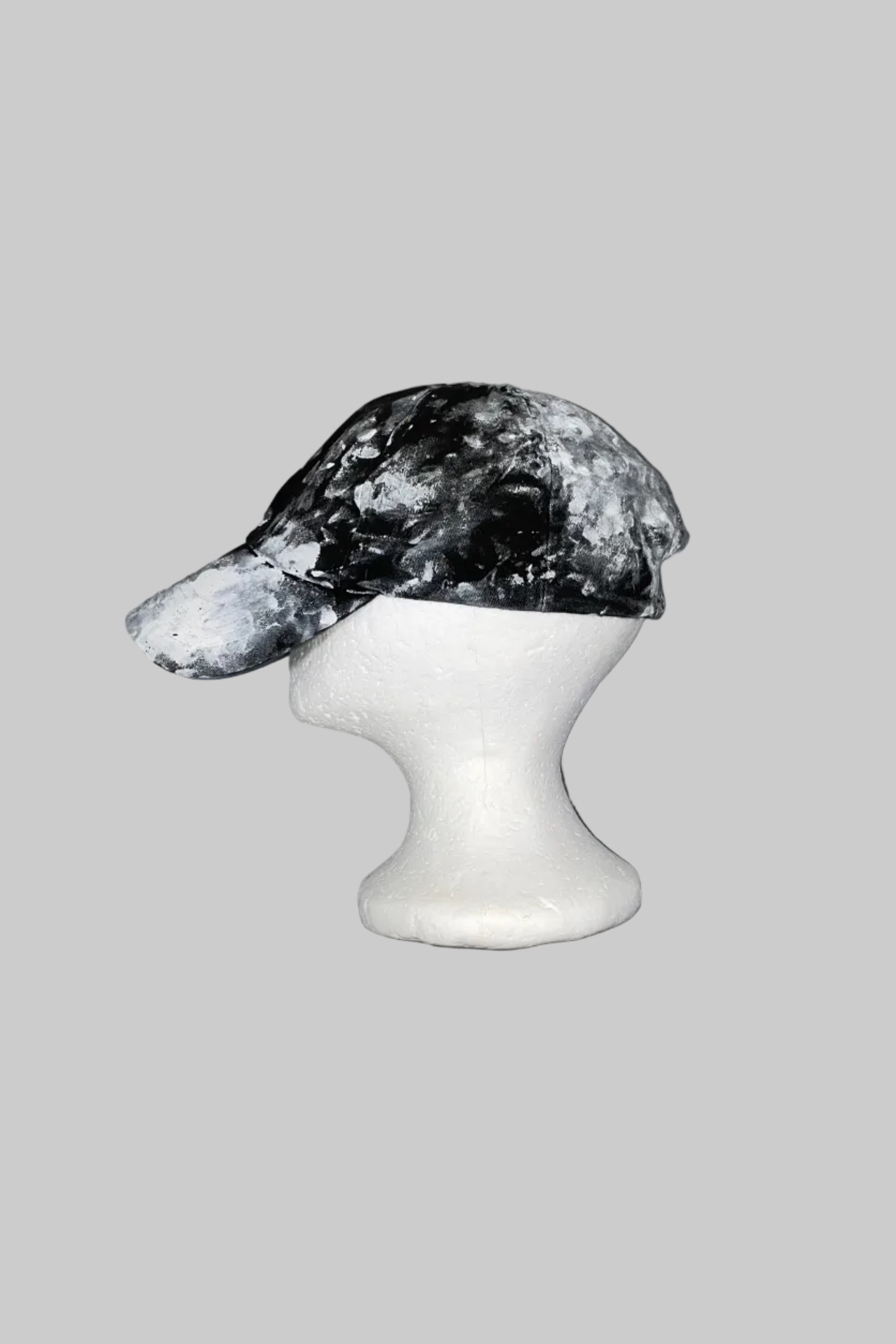 A black and white marbled or splattered baseball cap displayed on a white styrofoam mannequin head against a scratched gray background.